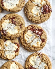 chocolate chip cookies with white butter and jelly on top sitting on wax paper, ready to be eaten