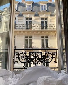 an open window with a view of a balcony and buildings in the background, looking out onto a bed