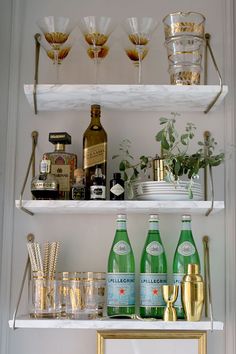 bottles and glasses are sitting on shelves in a room with white walls, gold trim