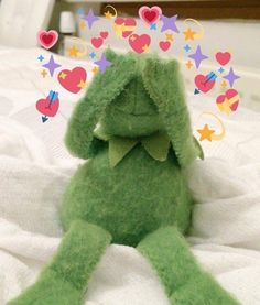 a green stuffed animal sitting on top of a white bed next to hearts and stars