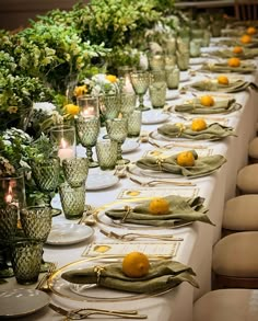 a long table is set with green and yellow place settings, glass vases filled with lemons and greenery