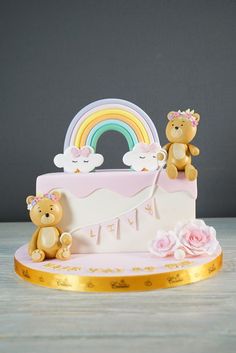 two teddy bears sitting on top of a pink cake with a rainbow in the background