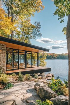 a house on the edge of a lake surrounded by trees and rocks with an open porch