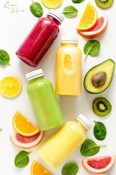 various fruits and juices are arranged on a white surface with green leaves, oranges, kiwi, and avocado