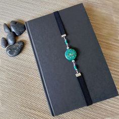 a book with a blue beaded bracelet on it next to some rocks and stones