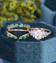 an engagement ring with green and white stones on the side, sitting on top of a velvet box