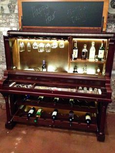 an old piano with wine bottles and glasses on it in front of a chalkboard