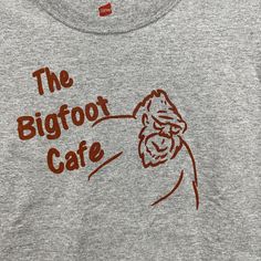 T-shirt, featuring a bigfoot sketch with The Bigfoot Cafe printed on the front in brown ink. This is an adult T-shirt in gray with the words The Bigfoot Cafe and a bigfoot printed with brown ink on the front. Hand printed at home with a manual screen press. If you prefer another color or size; Look around my shop, I may have what you are looking for. Bigfoot Sketch, Gender Neutral, I Shop, Sketch, Adult Outfits, Cafe, Tops & Tees, T-shirt, Top Outfits