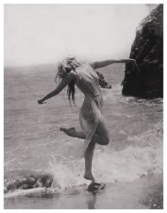 a woman standing on top of a wave covered beach next to the ocean with her arms outstretched