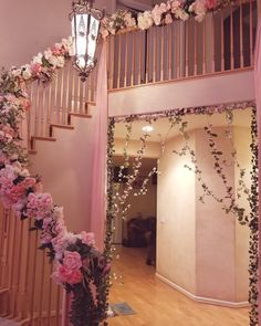 a staircase decorated with pink flowers and greenery next to a chandelier hanging from the ceiling