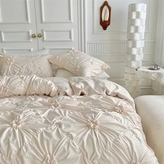 a bed with white comforters and pillows in a room next to a mirror on the wall