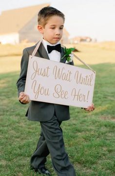 a young boy in a tuxedo holding a sign that says just wait until you see her