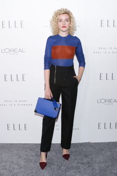 a woman with blonde hair wearing black pants and blue shirt holding a blue purse in her hand