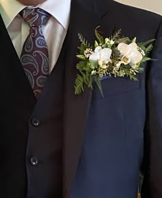 a man wearing a suit and tie with flowers on his lapel flower is seen in this image