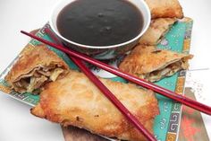 two pastries with chopsticks next to a bowl of dipping sauce on a plate