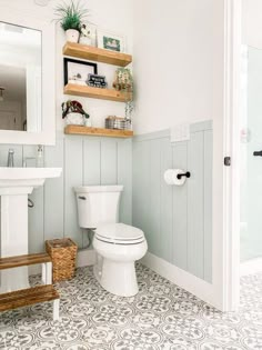 a white toilet sitting in a bathroom next to a sink under a mirror and wooden shelves