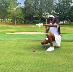 a woman kneeling down on the ground holding a golf club in one hand and a red ball in the other