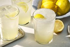 two glasses filled with lemonade next to some lemons