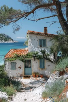 an old house sitting on top of a rocky hill next to the ocean with plants growing out of it