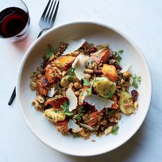 a white bowl filled with food next to a fork and glass of wine on top of a table