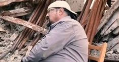 a man sitting on top of a wooden chair in front of a pile of rubble