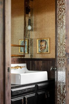 a bathroom sink sitting under a mirror next to a wooden wall with pictures on it