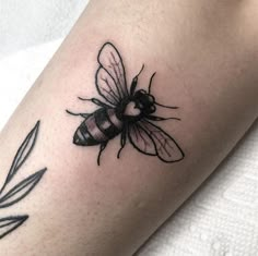 a black and white tattoo of a bee on the left arm with an olive branch