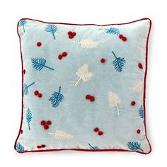 a blue pillow with white leaves and red berries on the front, sitting on a white surface