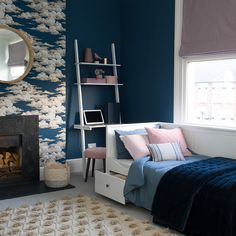 a bedroom with blue walls, white furniture and a pink chair in front of the fireplace