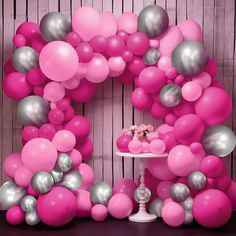 a table topped with a cake covered in pink and silver balloons next to a wall