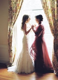 two women standing next to each other in front of a window with curtains on it