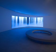 an empty room with a circular bench in front of a wall that has trees on it