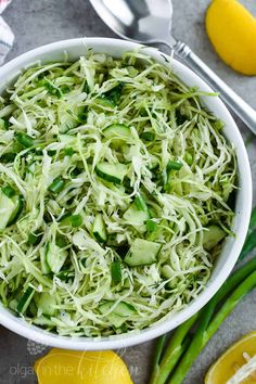 a white bowl filled with shredded cucumber and green onions next to lemons