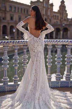 the back of a woman's wedding dress in front of a building and water