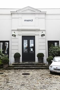 a white car is parked in front of a building with black doors and window frames