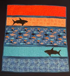 a quilted wall hanging with shark and fish on it's sides in different colors