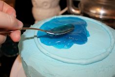 a person is spooning blue icing onto a cake