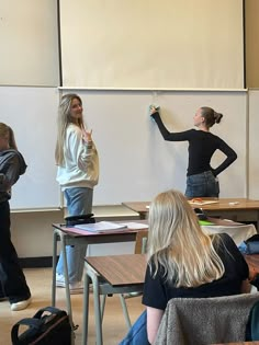 two girls are writing on a whiteboard while another girl is standing in front of them