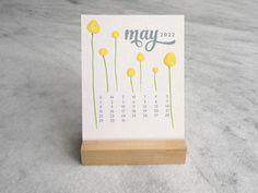 a calendar sitting on top of a wooden stand with yellow flowers in front of it