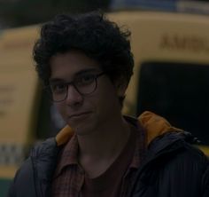 a young man with glasses is standing in front of a bus and looking at the camera