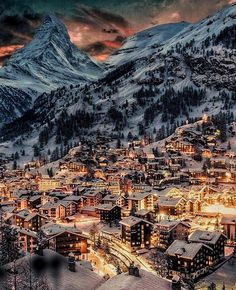 a town in the mountains covered in snow at night with lit up buildings and lights