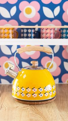 a yellow tea kettle sitting on top of a wooden table next to colorful wallpaper