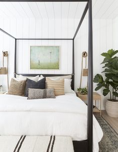 a bed with white sheets and pillows in a bedroom next to a potted plant