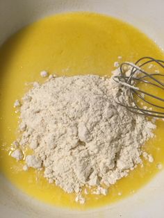 a bowl filled with yellow liquid and flour next to a whisk on top of it