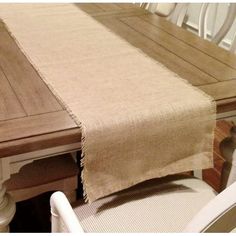 a wooden table with white chairs and a tan linen runner on it's edge