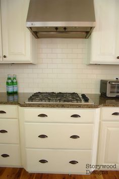 a stove top oven sitting inside of a kitchen next to white cabinets and wooden floors