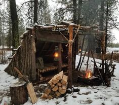 an outdoor shelter made out of logs in the snow with a lit lantern on top