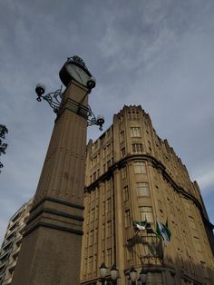 a tall building with a clock on the top of it's tower and two flags flying in front of it