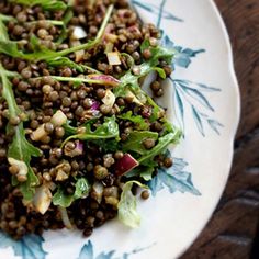 a white plate topped with lentils and green leafy greens on top of a wooden table