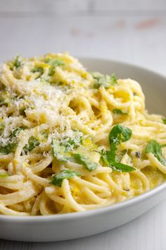 a white bowl filled with pasta covered in parmesan cheese and green leaves on top